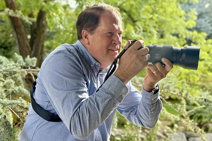 Scot Facer Proctor holding a camera with a telephoto lens outdoors, sharing his Sea of Galilee photography experience for the 2027 Come Follow Me Calendar.