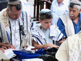 Jewish worshippers wearing tefillin and praying together as they recite the Shema Yisrael, illustrating the living tradition of Deuteronomy and covenant devotion.