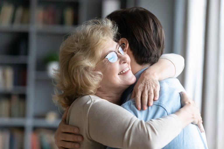 Elderly mother and adult son hugging at a family reunion.