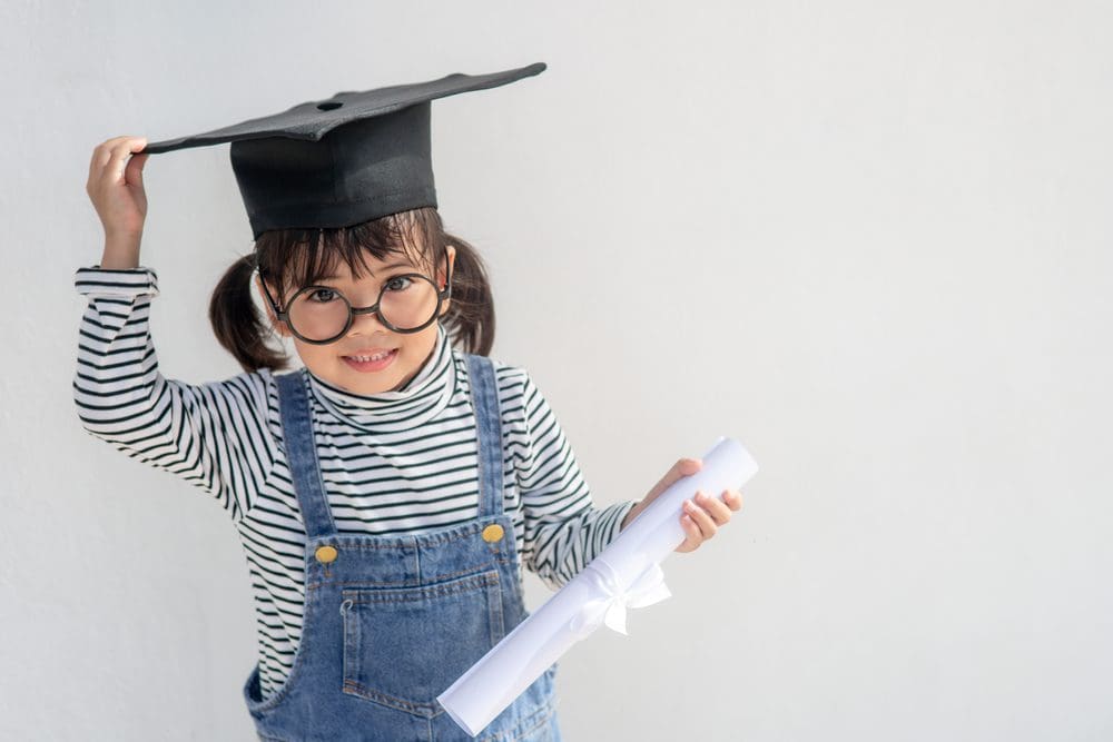 A happy young girl wearing a graduation cap and glasses, holding a diploma.