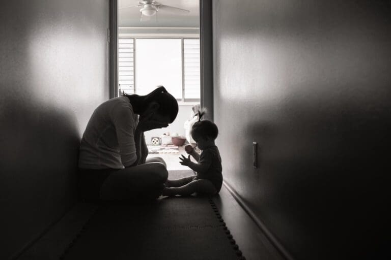A mother struggling emotionally sits in a hallway with her baby, capturing the challenges and emotions of motherhood.