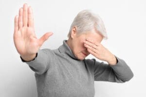 Woman raising hand and covering her face, symbolizing the difficulty of saying no and setting boundaries.
