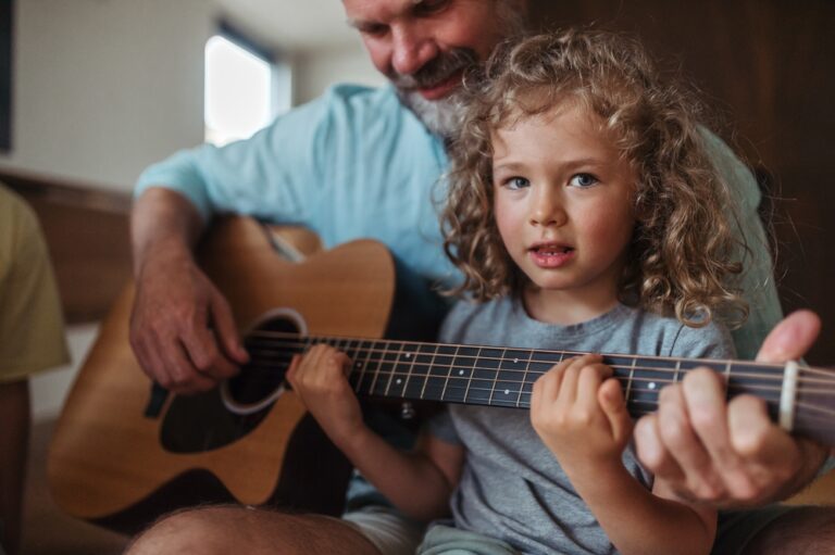 Child and elder playing acoustic guitar together in a warm setting.