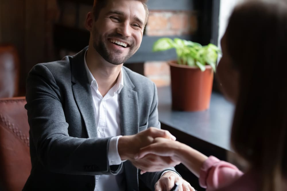 Smiling man in a sport coat shaking hands with a woman in a café, representing the start of a meaningful relationship in the Latter-day Saint mid-singles community.