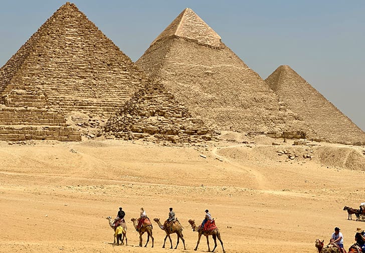  Camels and their riders travel across the desert sands toward the pyramids of Giza, capturing the timeless allure of ancient Egypt.