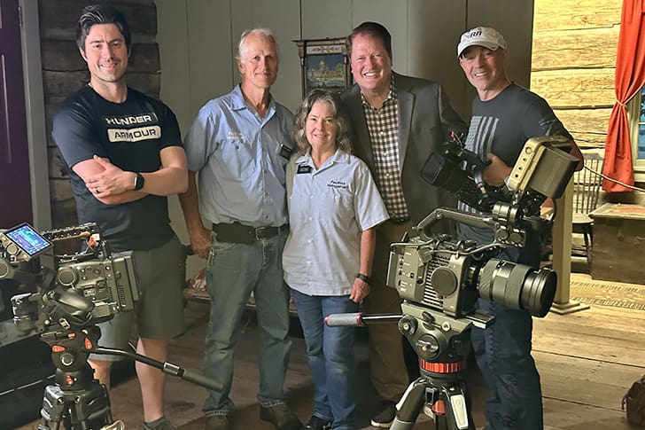  A group of videographers and Scot pose together inside a historic LDS Church site, surrounded by professional filming equipment.