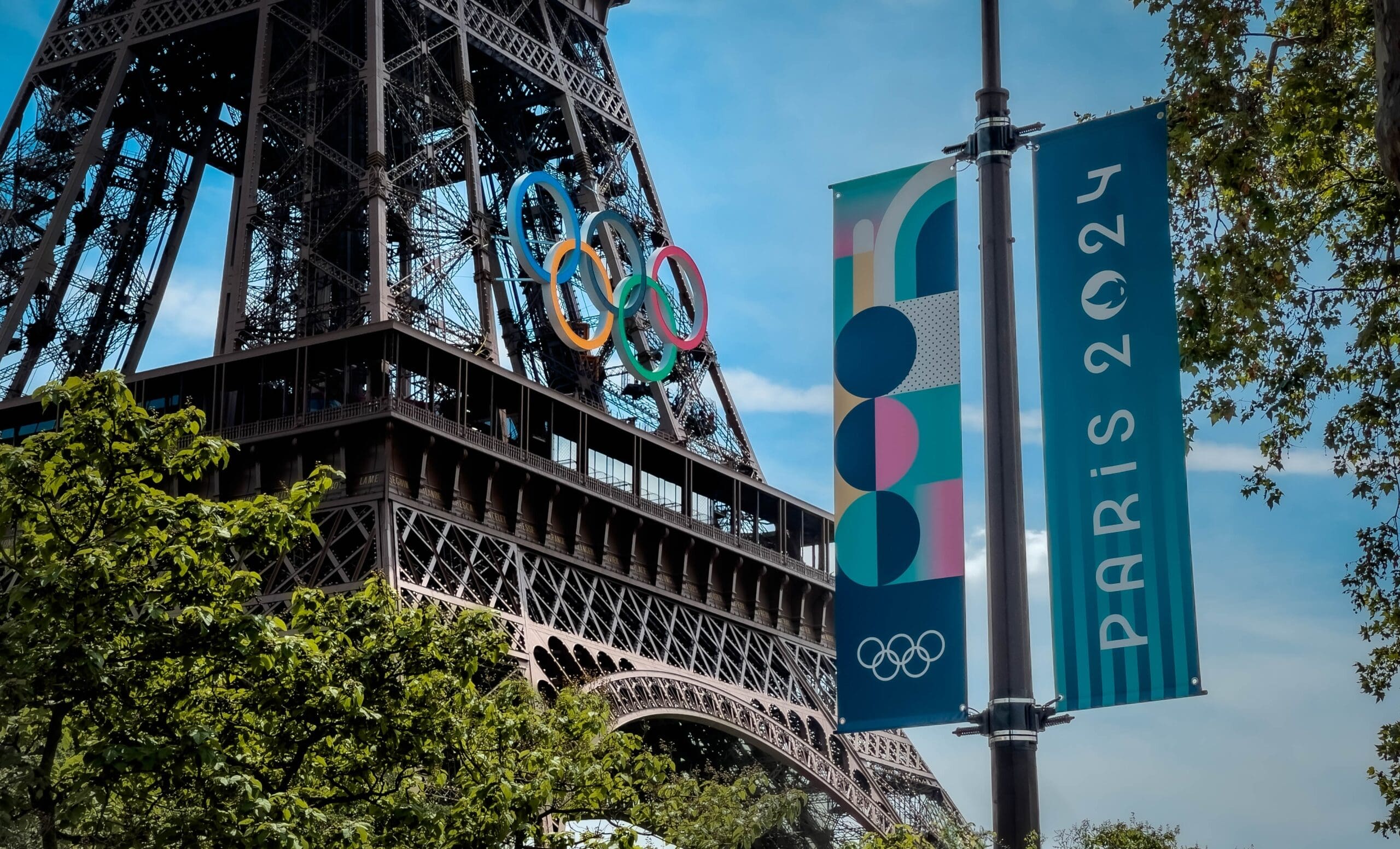 Eiffel Tower with Olympic rings and Paris 2024 banner in the foreground.
