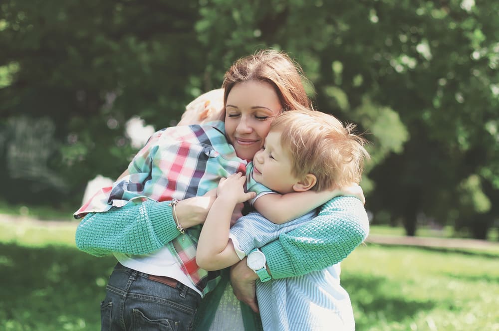 Mother hugging two children in a park, symbolizing calm and consistent parenting without emotional triggers.