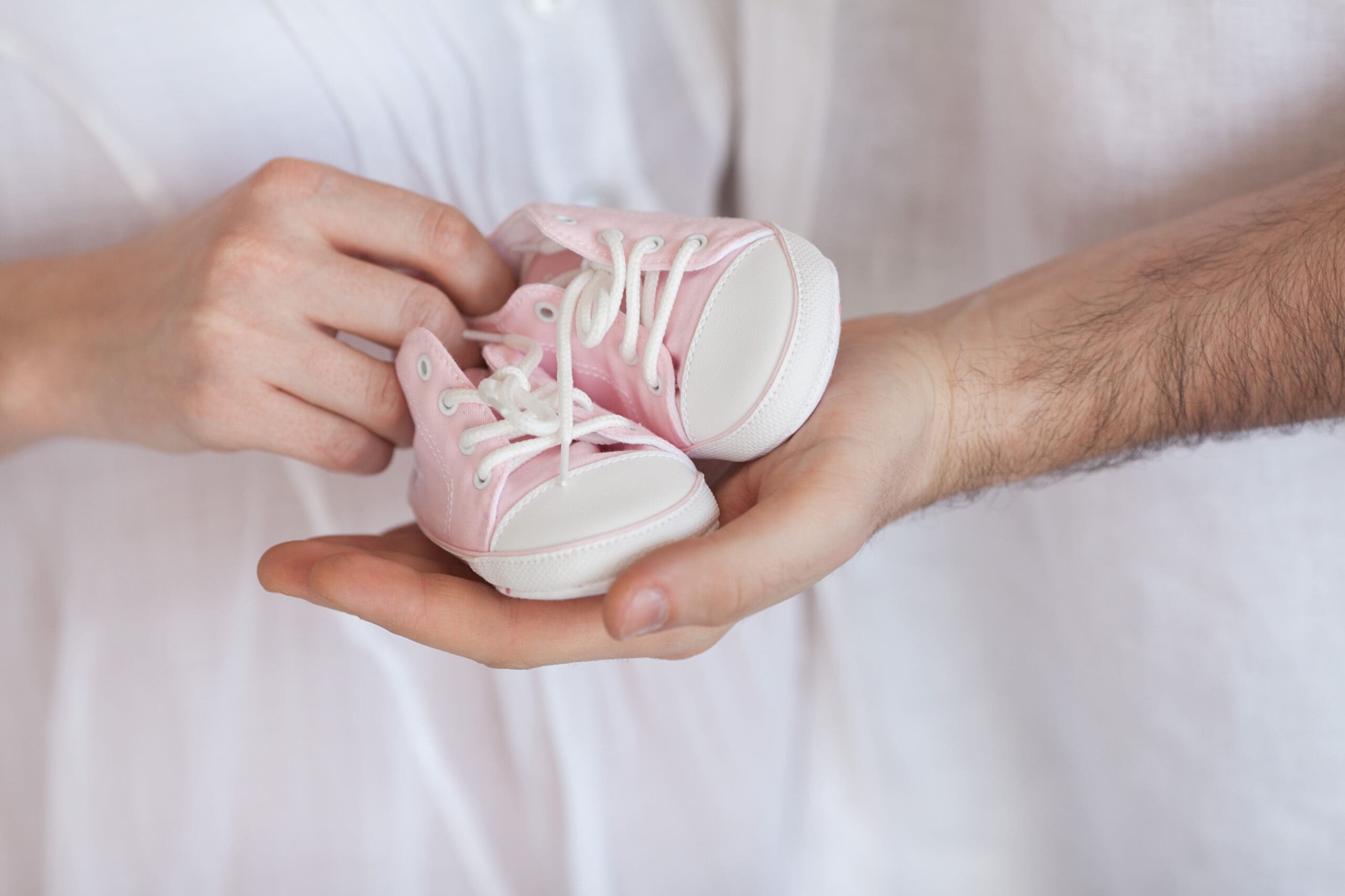 Pink baby shoes held by parents, representing pregnancy loss and eternal implications in LDS doctrine.