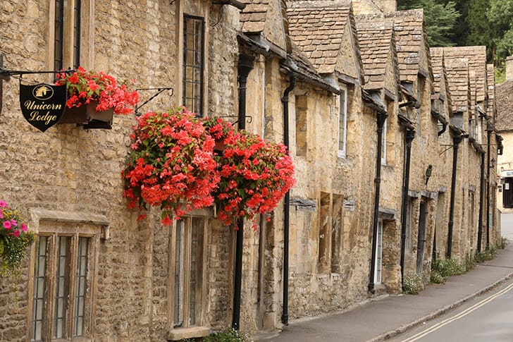 A picturesque street in Castle Combe, adorned with vibrant flowers and traditional stone cottages, capturing the quintessential Cotswolds aesthetic.