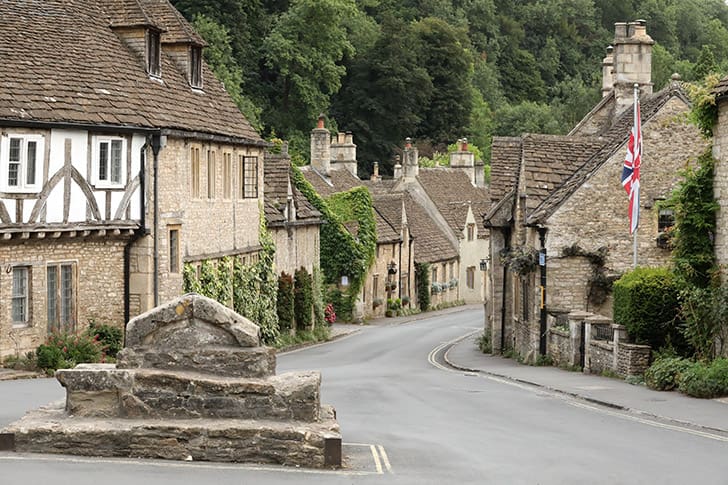 Castle Combe’s quiet village road, with stone houses and the Union Jack flag waving, showcases the tranquil beauty of the Cotswolds.