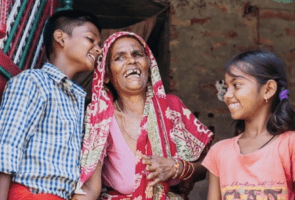 Grandmother with two smiling children in a leprosy colony in India.