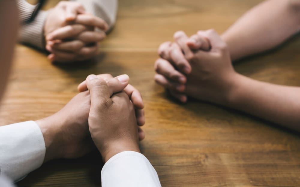 Hands clasped in prayer at a table symbolizing unity and spiritual growth.