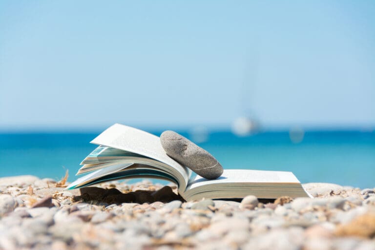 Open book on beach with a stone, symbolizing adventure and escapism in reading.