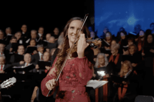 Violinist performing with a choir during "Joy to the World" Christmas concert.