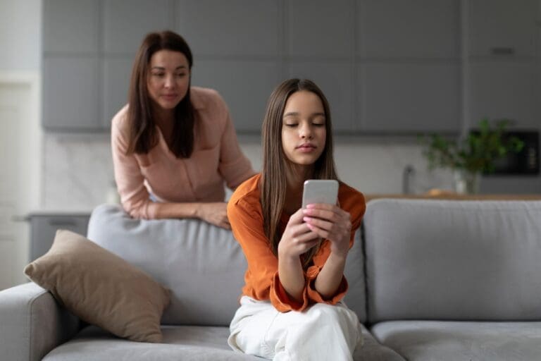 Mother watching teenage daughter on phone, symbolizing parenting and trust-building.