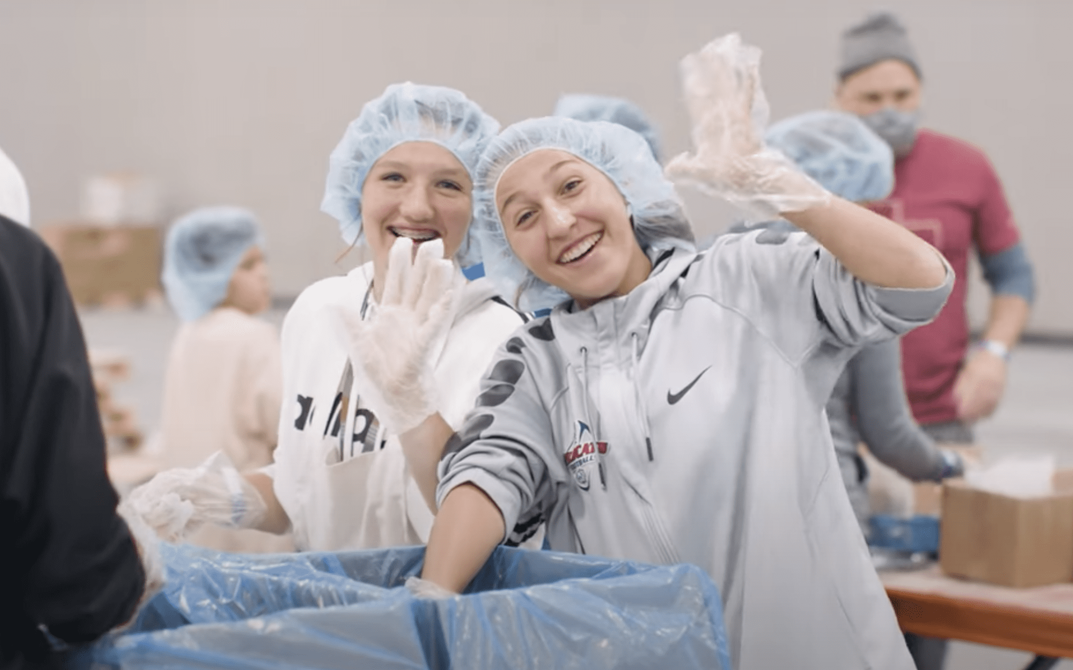 Youth volunteers wearing gloves and hairnets, smiling while packing meals for the Utah Food Bank during the Silicon Slopes service project.