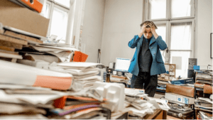 Person overwhelmed by clutter in a messy office, representing emotional clutter blocks and the need for a clutter-free lifestyle.