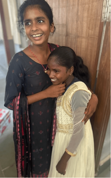 Two young girls embrace with bright smiles, celebrating friendship and newfound hope at the Rising Star Outreach school.
