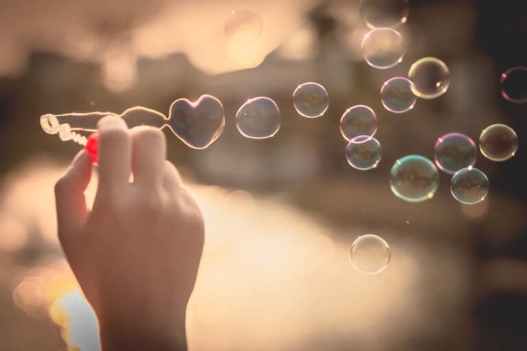 Hand blowing heart-shaped bubbles in the sunlight, representing joy, gratitude, and faith in Christ amidst life’s challenges.
