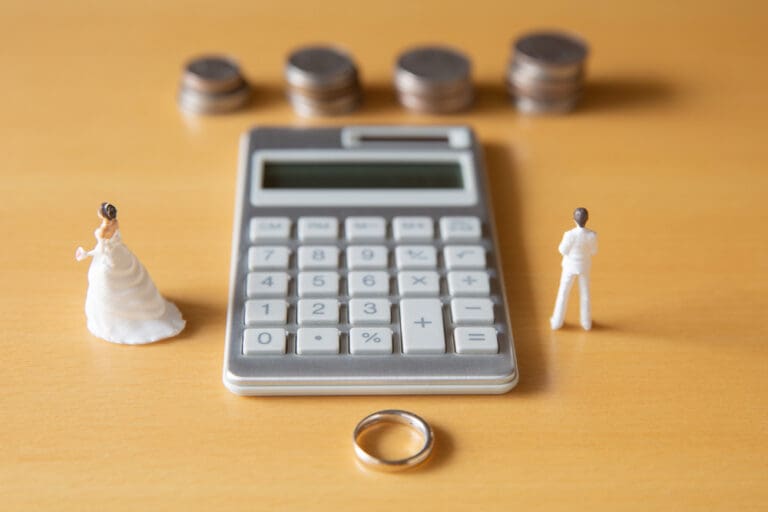 Financial impact of divorce with calculator, wedding ring, and figurines.
