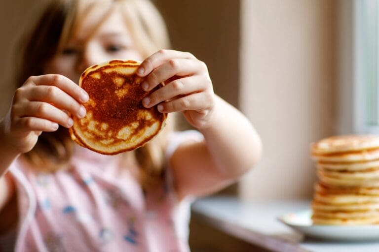 A child holding a pancake, representing the importance of developing a healthy relationship with food from a young age.