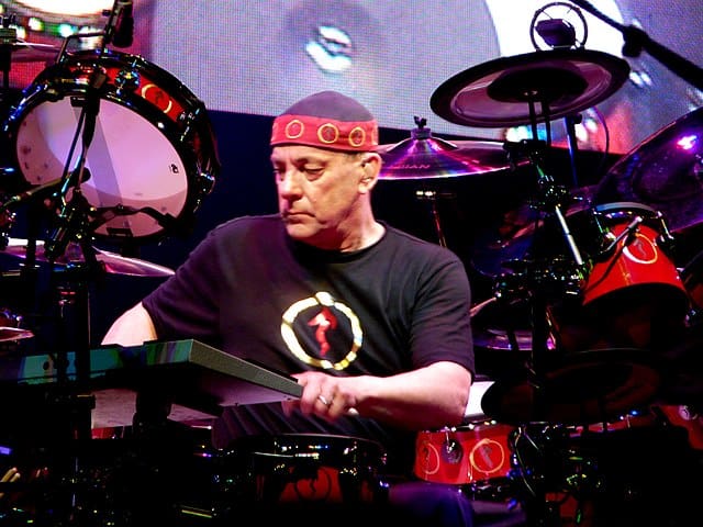 Neil Peart performing live on stage with Rush, surrounded by his drum set.