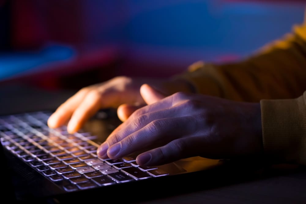 Hands typing on a keyboard in low light symbolizing the hidden nature of online pornography and digital sexual exploitation.