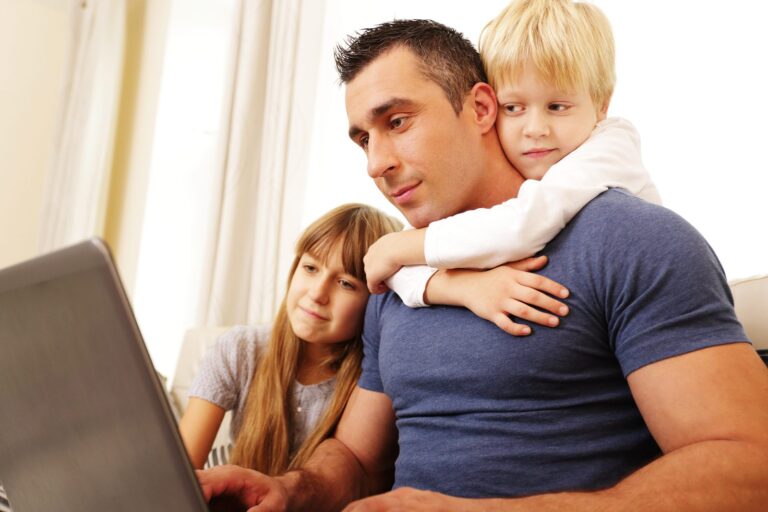 Father with two children looking at laptop together, representing healthy family boundaries and support in adult children’s relationships.