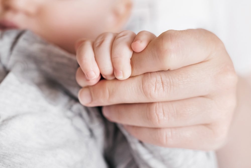 Baby holding parent’s finger, representing the value of children and the cultural shift needed to reverse declining fertility rates.