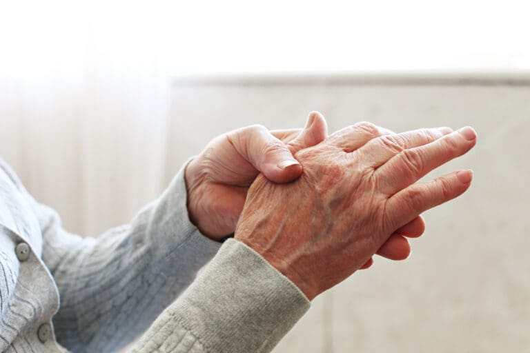 Elderly woman’s hands folded in reflection, symbolizing caregiving and aging