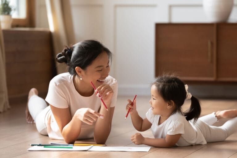 Mother and daughter smiling while drawing together on the floor, illustrating parenting with purpose and building meaningful relationships.