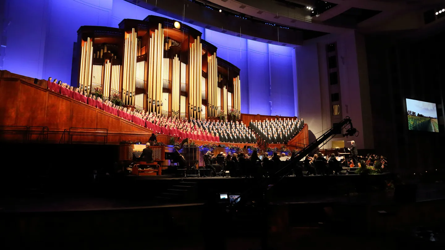 The Tabernacle Choir at Temple Square performing with full orchestra under blue lights in the Salt Lake Tabernacle for a Music & the Spoken Word broadcast.