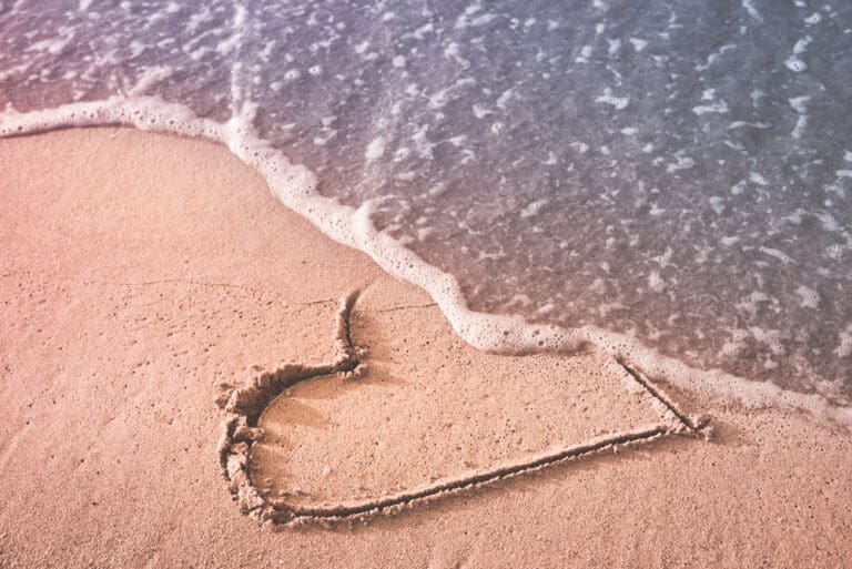 Heart drawn in beach sand being washed away by waves, symbolizing mid-singles healing after divorce and emotional rejection.
