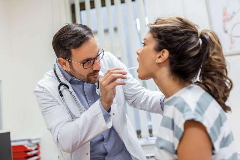 Doctor examining woman’s throat for upper respiratory infection during cold and flu season.