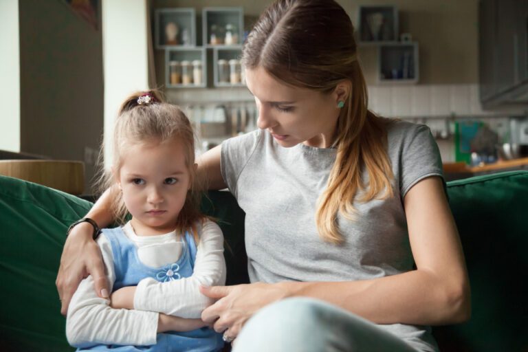 Mother calmly correcting upset daughter on couch, modeling confident parenting and loving discipline