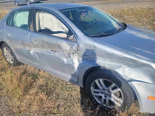 A silver sedan with major side damage sits in dry grass off the highway after a serious accident involving teens. The car shows visible dents and scraped metal from the impact described in Daris Howard’s story about miracles and trauma following a high-speed collision.
