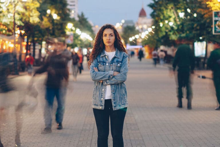Woman standing still on a busy street representing slowing down to gain wisdom through experience and service.
