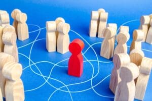 Isolated red wooden figure surrounded by family groups, symbolizing disconnection and outsider status in extended family dynamics.