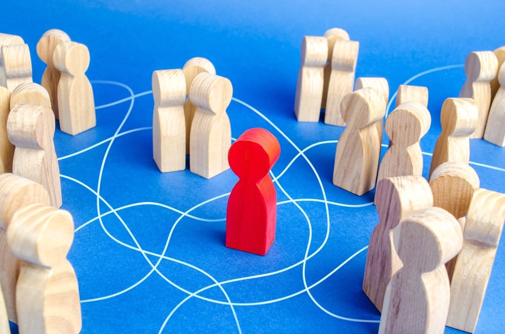 Isolated red wooden figure surrounded by family groups, symbolizing disconnection and outsider status in extended family dynamics.