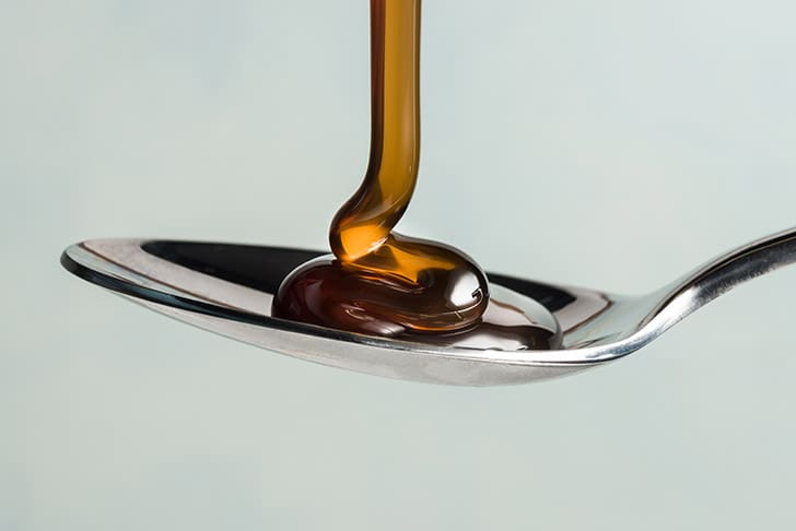 Thick syrup being poured onto a spoon, symbolizing the hidden sugars like corn syrup and fructose found in many hospital-issued shakes.