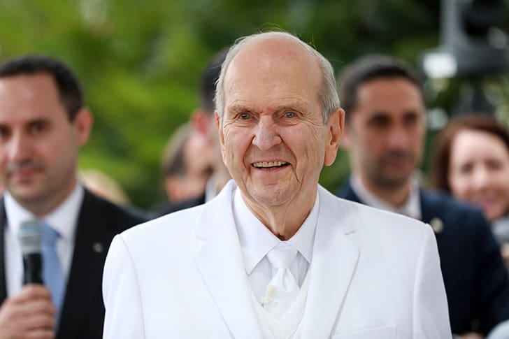 With a radiant smile, President Russell M. Nelson stands outside a temple, reflecting his Christlike leadership and prophetic call to think celestial and follow Jesus Christ.
