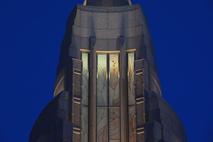 Temple spire with illuminated stained glass windows at night, highlighting teachings of President Russell M. Nelson on temple worship and discipleship.
