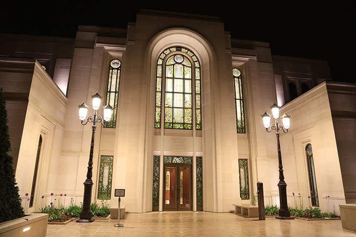 Paris Temple at night with stained glass windows aglow, symbolizing the light of Christ and temple blessings emphasized in President Nelson’s teachings.