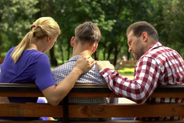 Parents comfort son on a park bench, reflecting courage and compassion in Tyler Robinson’s father urging his son to surrender after Charlie Kirk shooting