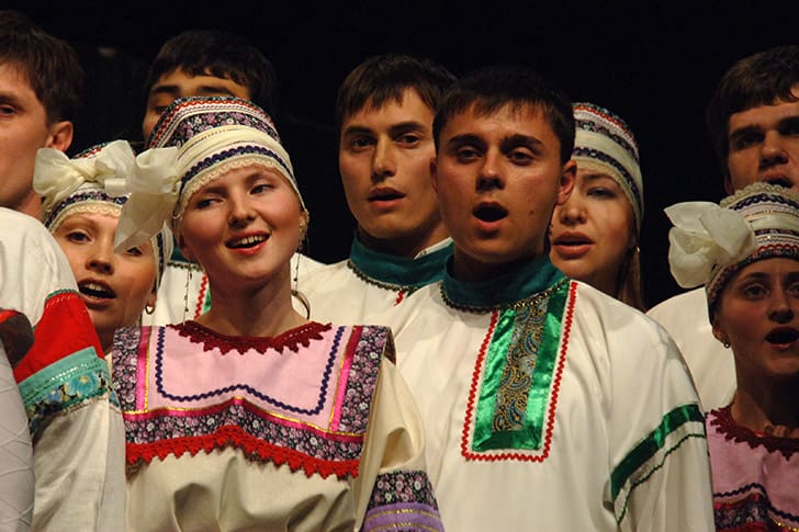 A diverse group of people dressed in traditional attire joyfully singing together, symbolizing the global gathering of Israel and unity in faith.