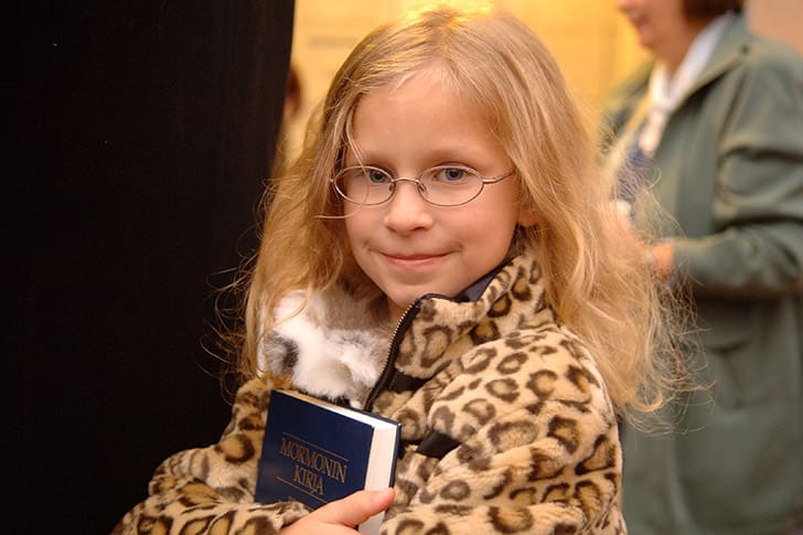 A young girl holds the Book of Mormon in her arms, representing how the Restoration scripture is central to the gathering of Israel.