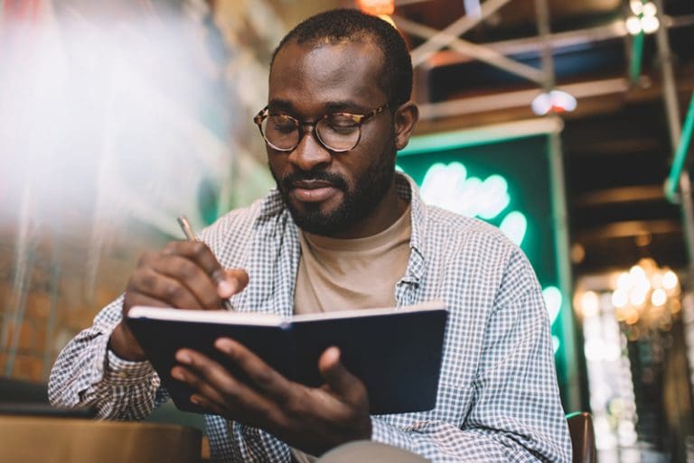Man writing in a personal journal to record moments that mark history such as 9/11, Charlie Kirk, and family history reflections.