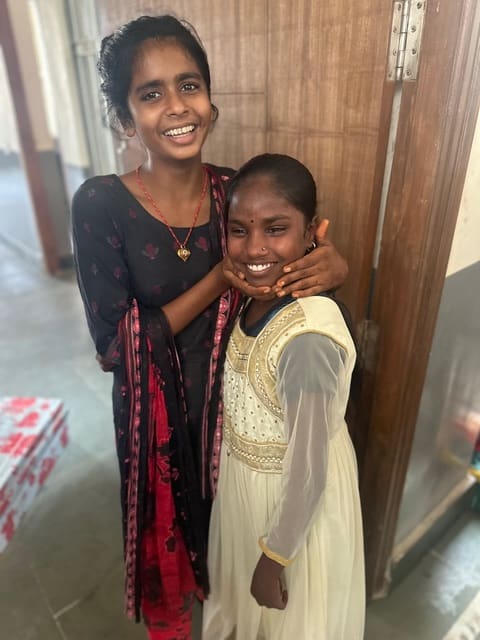 Two smiling girls embrace at Rising Star Outreach in India, celebrating Lakshmi’s miraculous recovery from leprosy. Their joy reflects faith, love, and healing through the Missionaries of Charity and Mother Teresa’s hospital.