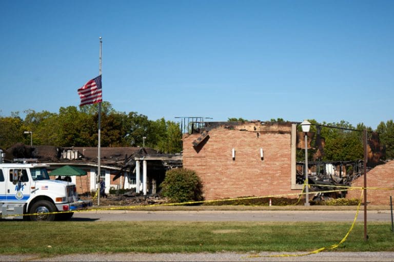 Burned Latter-day Saint chapel in Grand Blanc, Michigan, with flag at half-staff following church shooting and arson.